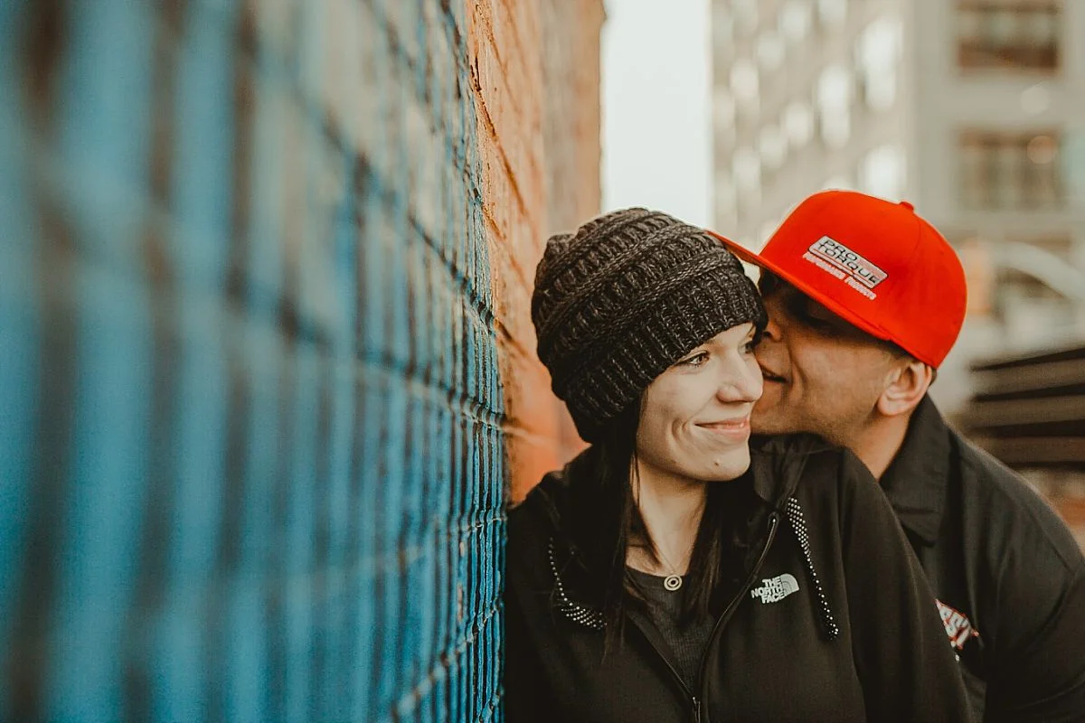 couple giggles while leaning against graffiti mural in brooklyn. photo by nyc family photographer krystil mcdowall