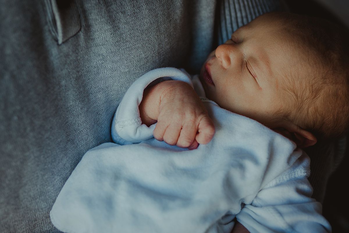 fresh 48 photo of newborn baby boy face snuggled in his dad's arms during fresh 48 photo shoot in nyc hospital when baby was 2 days old. photo by nyc family and newborn photographer krystil mcdowall