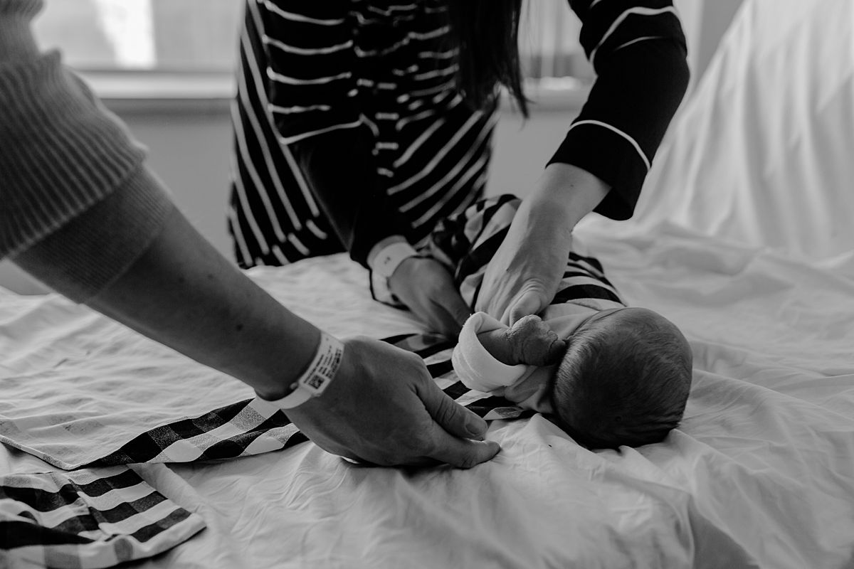 candid black and white fresh 48 photo of 2 day old newborn baby boy being swaddled by his parents in black and white swaddle. photo by nyc family and newborn photographer krystil mcdowall