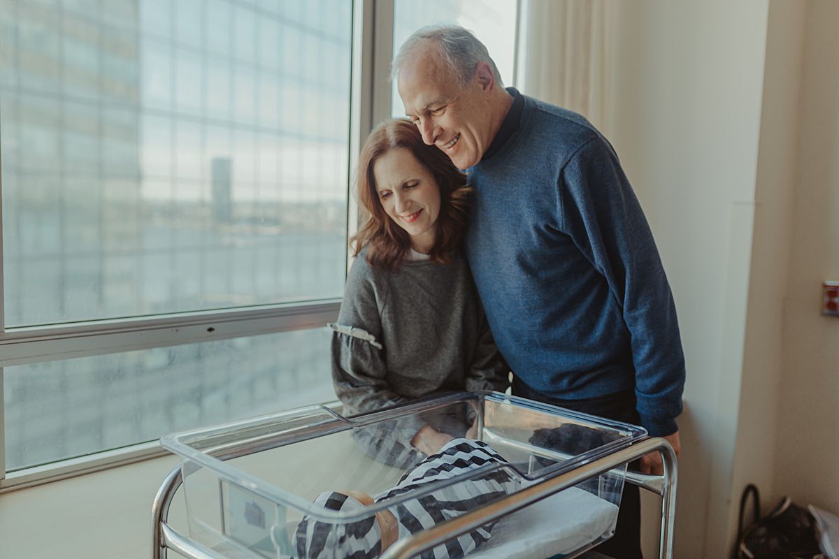 grandparents looking on as newborn grandson sleeps in his hospital bassinet. photo by nyc family and newborn photographer krystil mcdowall