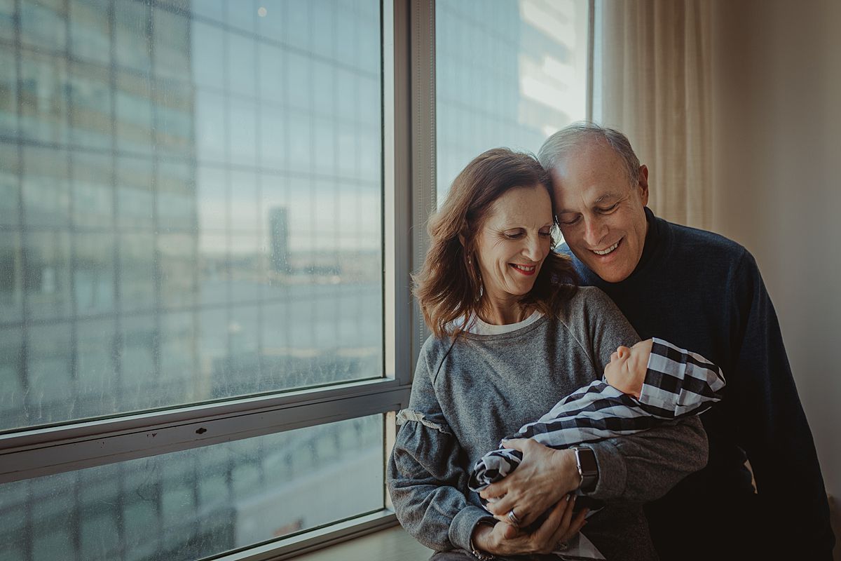 grandparents holding newborn grandson as sleeps in their arms in nyc hospital. photo by nyc family and newborn photographer krystil mcdowall