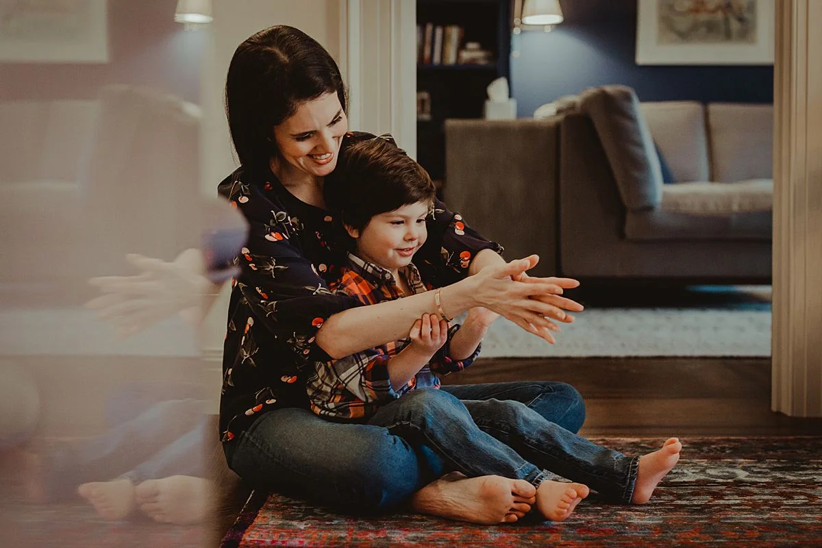 son sits on mom's lap playing hand games in living room of nyc apartment. NYC family photographer Krystil McDowall captures real family moments