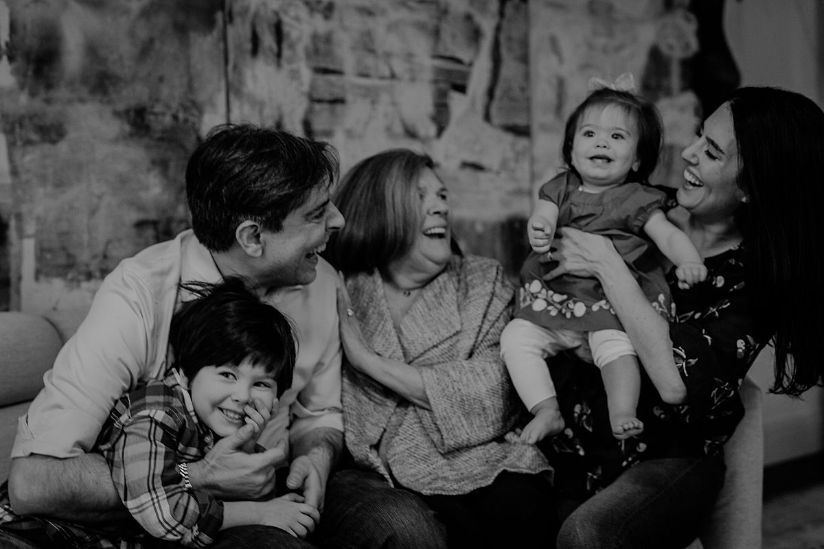 candid family portrait of one year old, big brother, dad and grandmother enjoying laughter and cuddles on the couch. photo by nyc family and newborn photographer Krystil McDowall