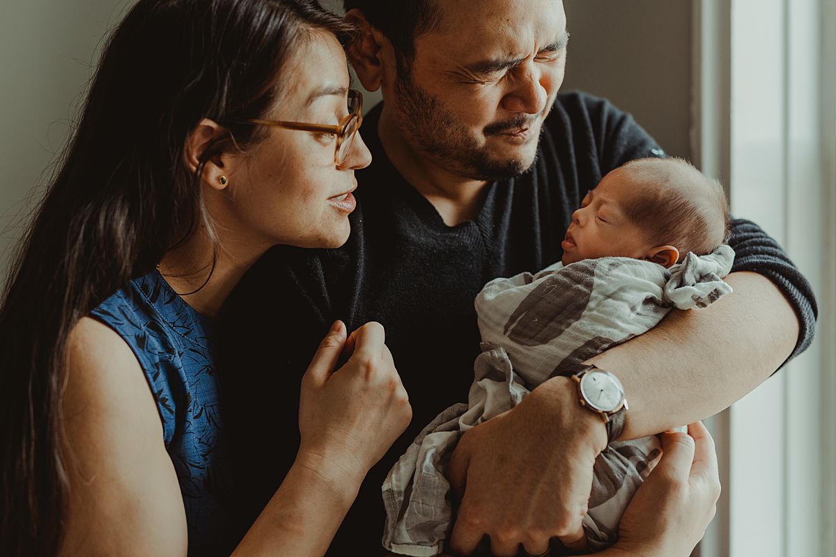 portrait of mom and dad holding newborn son and making silly faces in nyc apartment. photo by nyc family and newborn photographer krystil mcdowall