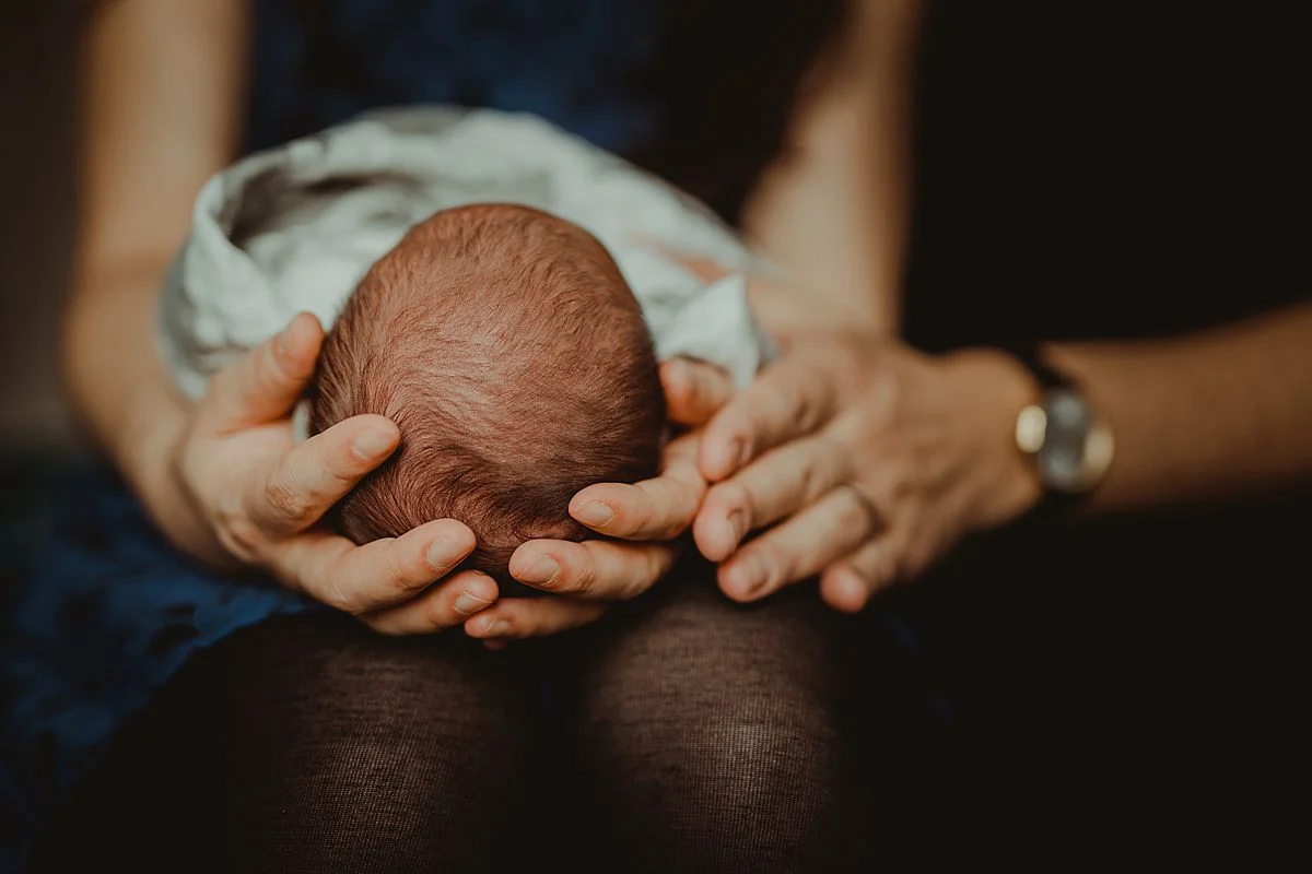 close up photo of mom holding newborn son on her lap while sitting on bed in nyc apartment. photo by nyc family and newborn photographer krystil mcdowall