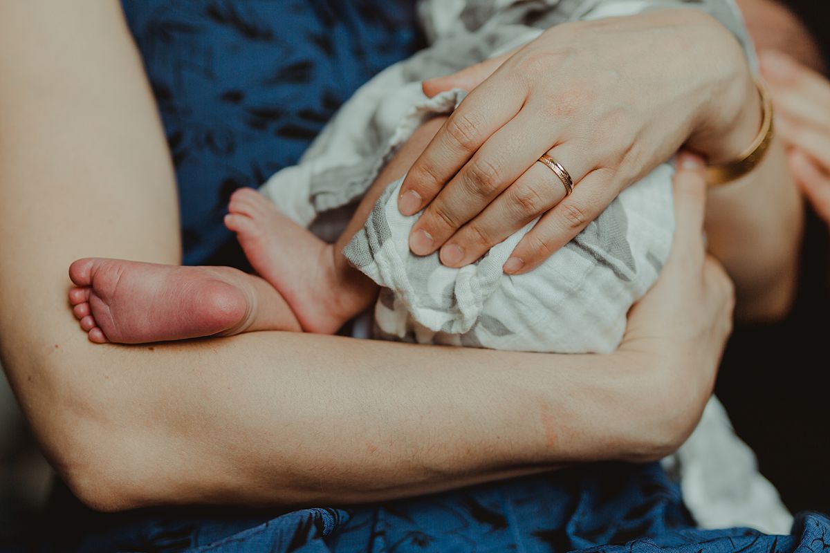 close up photo of mom holding newborn son while wrapped in whale swaddle and son's feet hanging outside off swaddle. photo by nyc family and newborn photographer krystil mcdowall