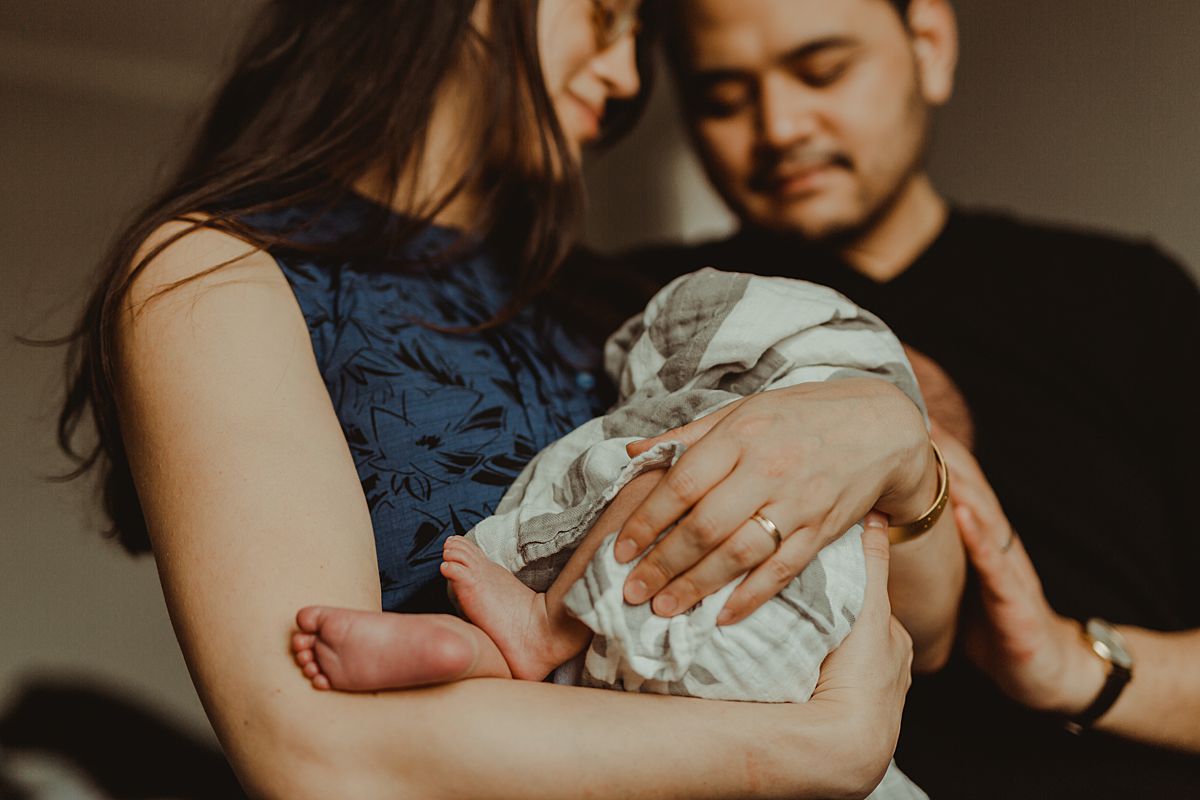 close up photo of mom holding newborn son while wrapped in whale swaddle and son's feet hanging outside of swaddle while mom and dad dotingly look at son. photo by nyc family and newborn photographer krystil mcdowall