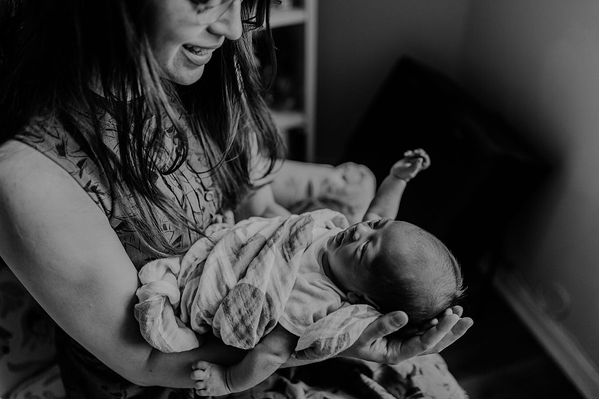 monochrome photo of mom sitting in antique chair holding newborn son and making sweet faces at him. photo by nyc family and newborn photographer krystil mcdowall