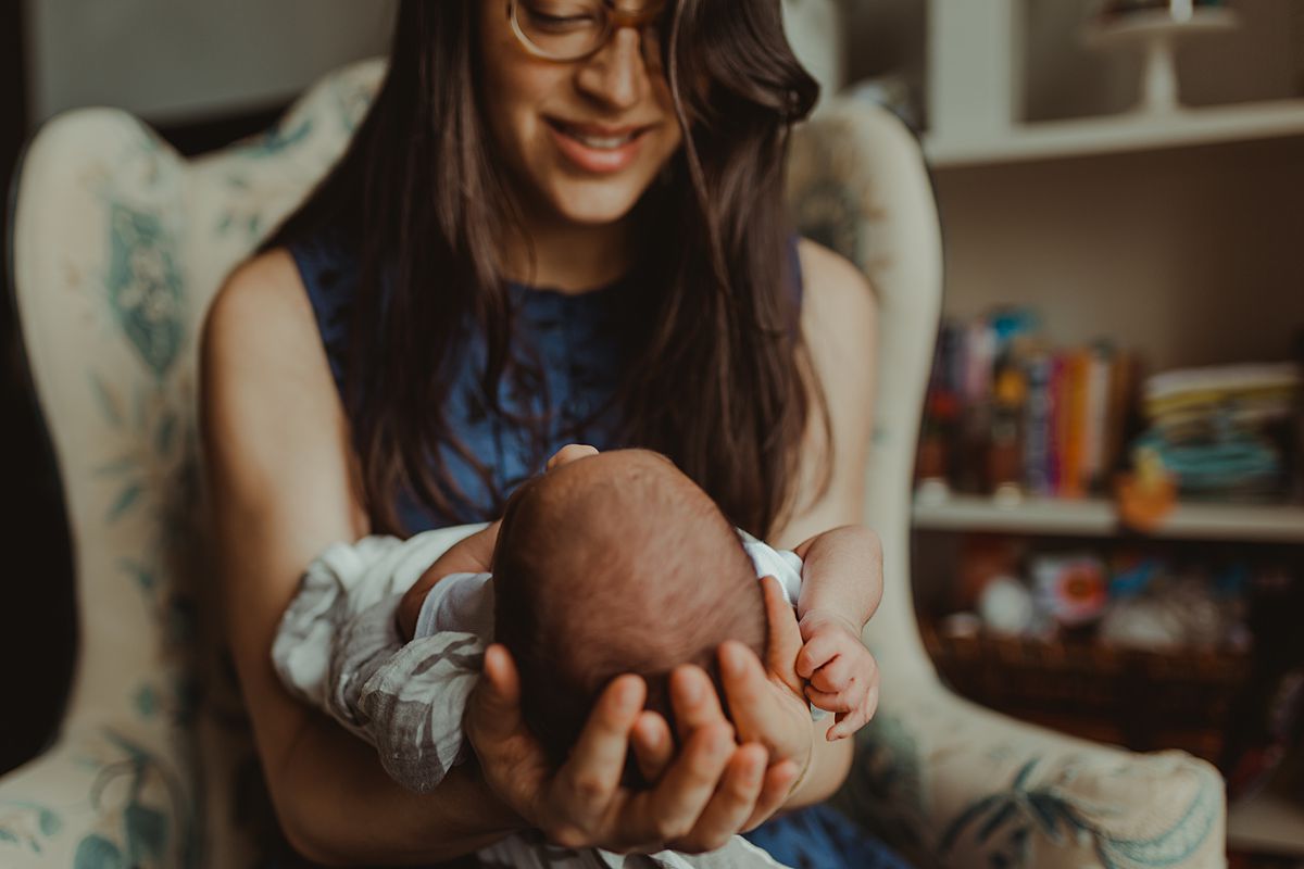 portrait of mom sitting in antique chair in nyc lounge room holding newborn son. photo by nyc family and newborn photographer krystil mcdowall