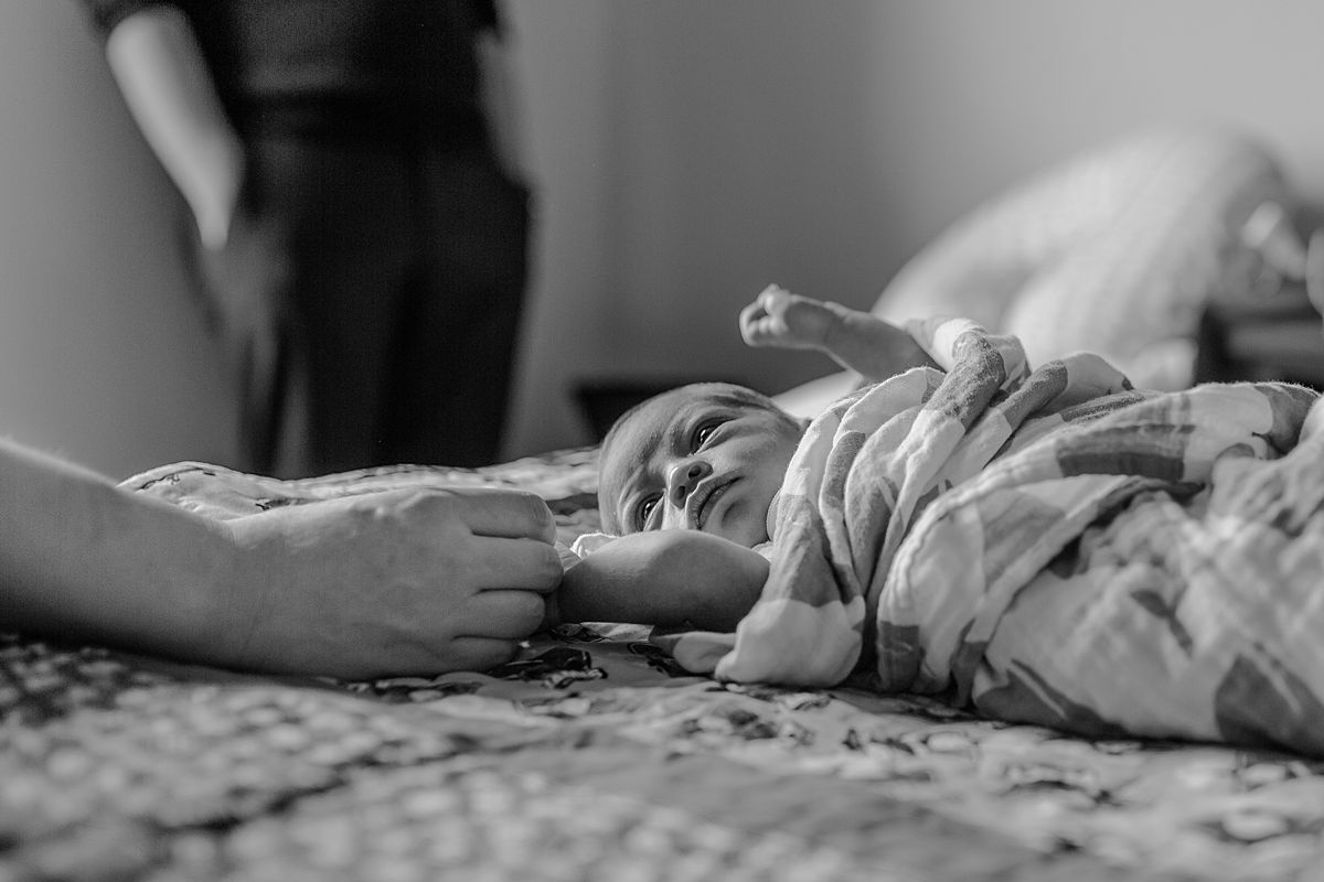 photo of mom holding newborn son's hand as he lays on parents bed and look up a his mom with big wide eyes. photo by nyc family and newborn photographer krystil mcdowall