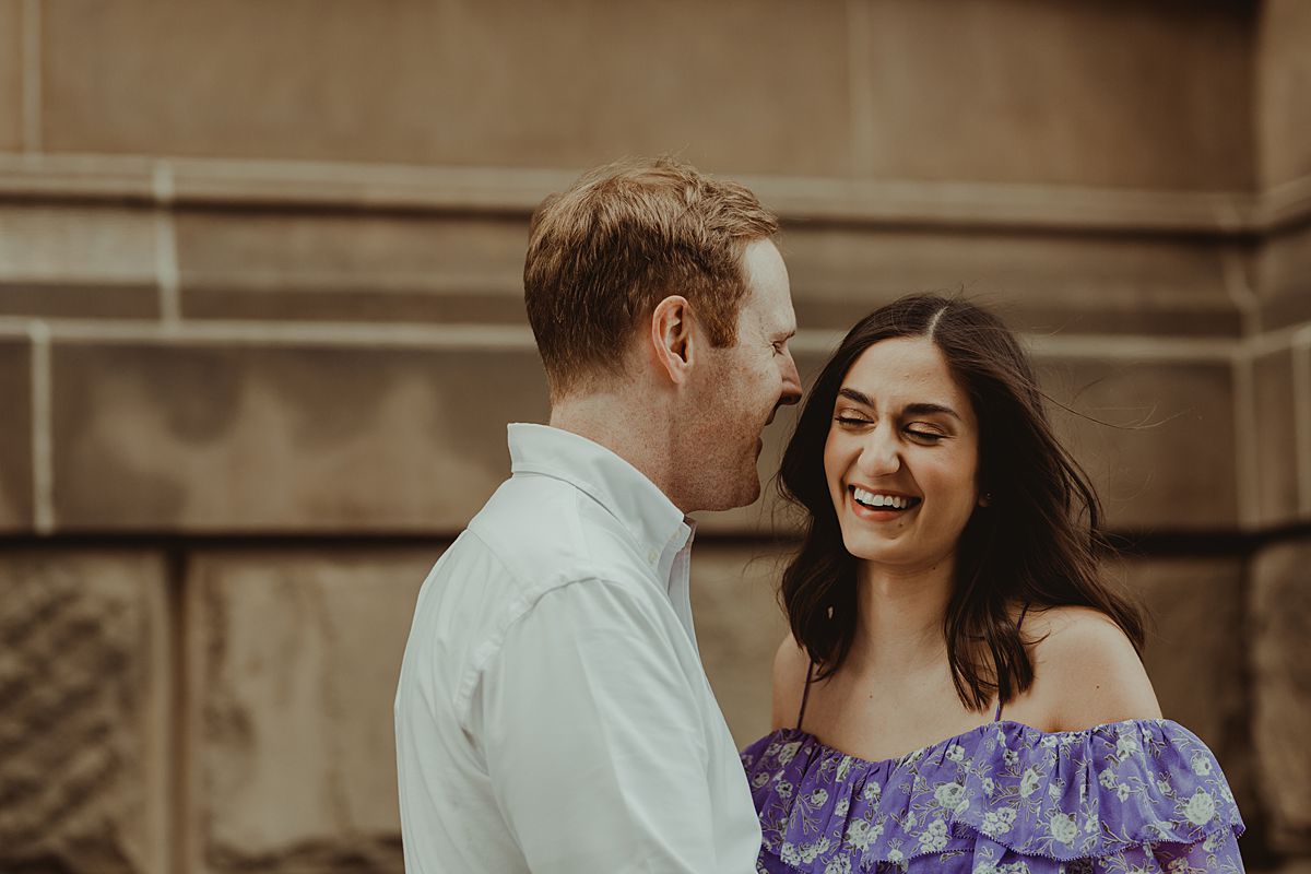 expecting couple happily giggling in front of The Dakota on central park west nyc during maternity photo session. maternity photo by nyc family and newborn photographer krystil mcdowall