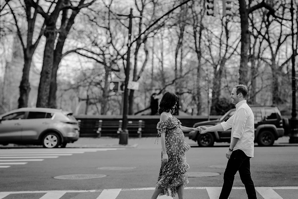 black and white lifestyle photo of expecting couple walking along central park west during their maternity photo session. image by nyc family and newborn photographer krystil mcdowall