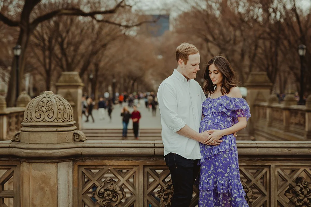 expecting couple stands at bethesda terrace in central park new york city holding mom's expecting belly. image by nyc family and newborn photographer krystil mcdowall