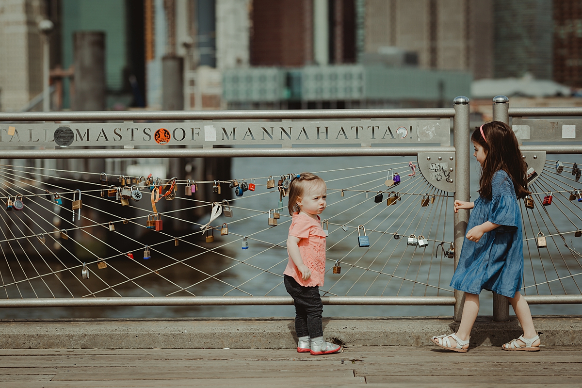 two daughters playing with the love locks at the brooklyn bridge park with manhattan skyline in the background. photo by nyc family and newborn photographer krystil mcdowall