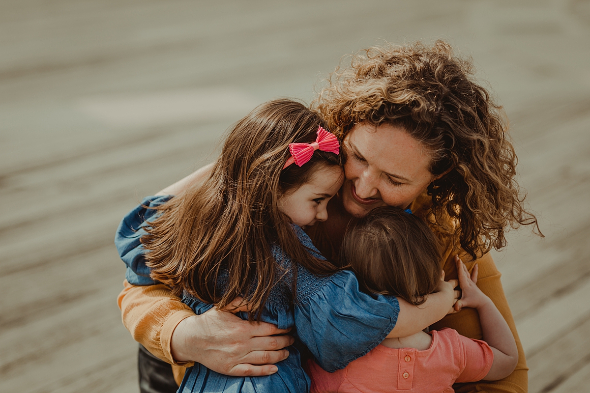photo of mom hugging both her daughters at the pier at brooklyn bridge park. photo by nyc family and newborn photographer krystil mcdowall