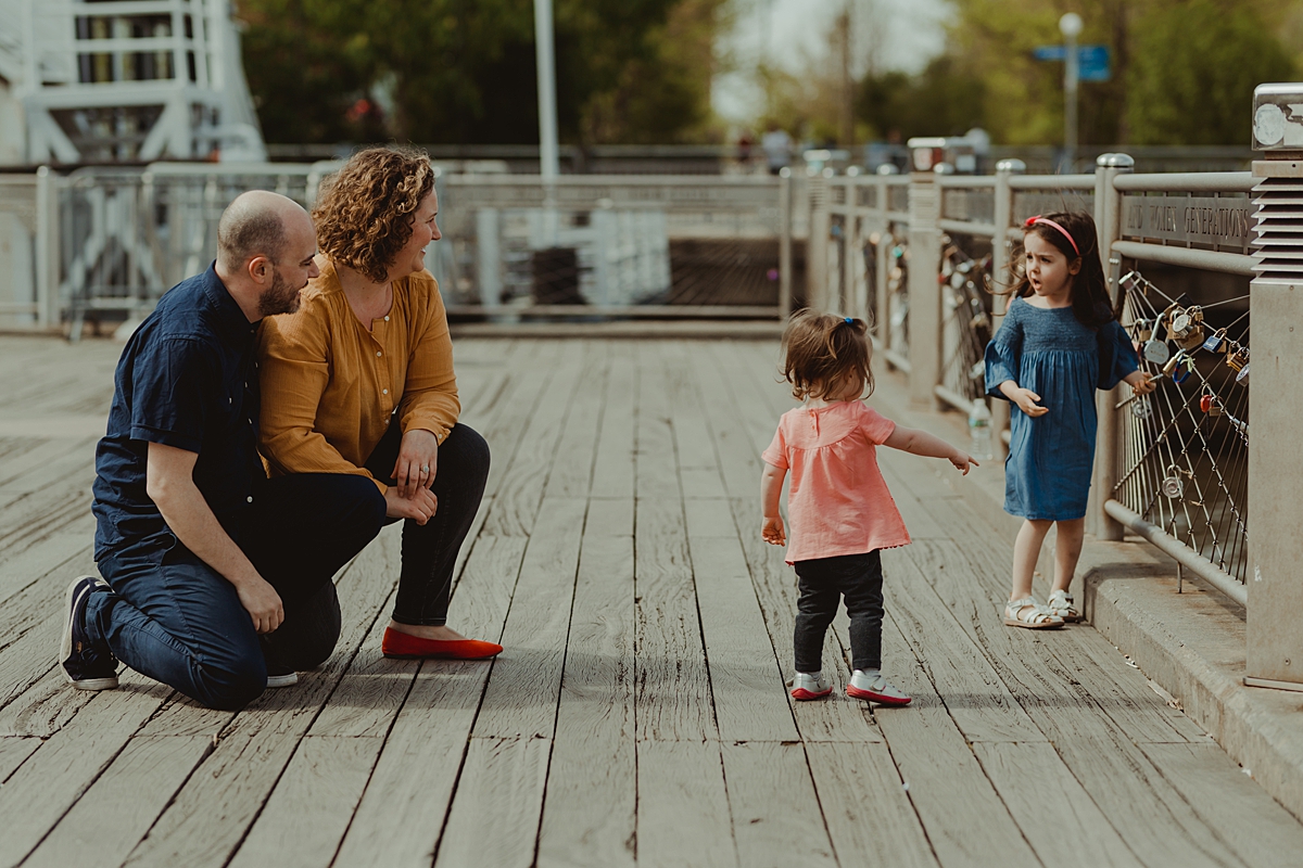 candid photo of family of four playing on the pier at brooklyn bridge park. photo by nyc family and newborn photographer krystil mcdowall