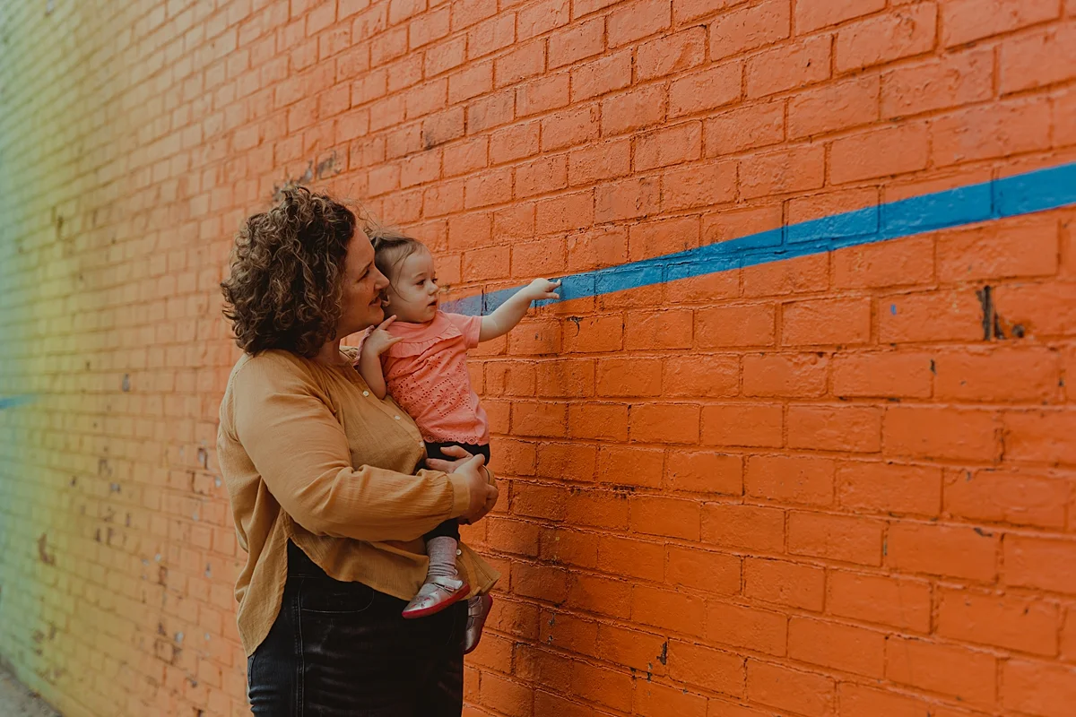 photo of mom and youngest daughter standing in front of bright orange graffiti wall in dumbo brooklyn. photo by nyc family and newborn photographer krystil mcdowall