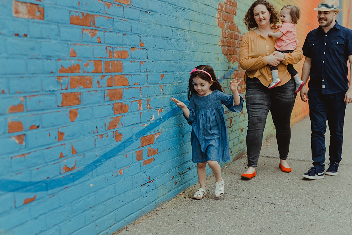 photo of family strolling in front of colorful graffiti wall during fun filled family photo session in new york city. photo by nyc family and newborn photographer krystil mcdowall