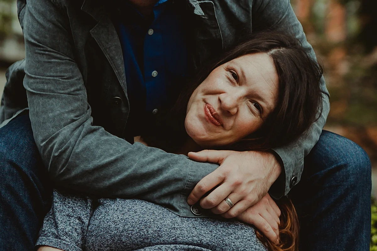 portrait of expecting mom smiling for the camera while her husband's arms are wrapped around her for a hug. photo by nyc family and newborn photographer krystil mcdowall