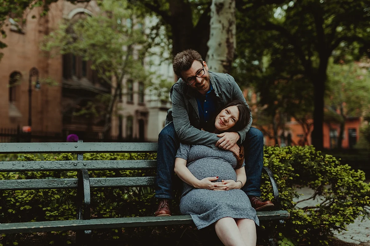 photo of expecting husband and wife sitting on park bench in stuyvesant square during maternity photo session in nyc. photo by nyc family and newborn photographer krystil mcdowall