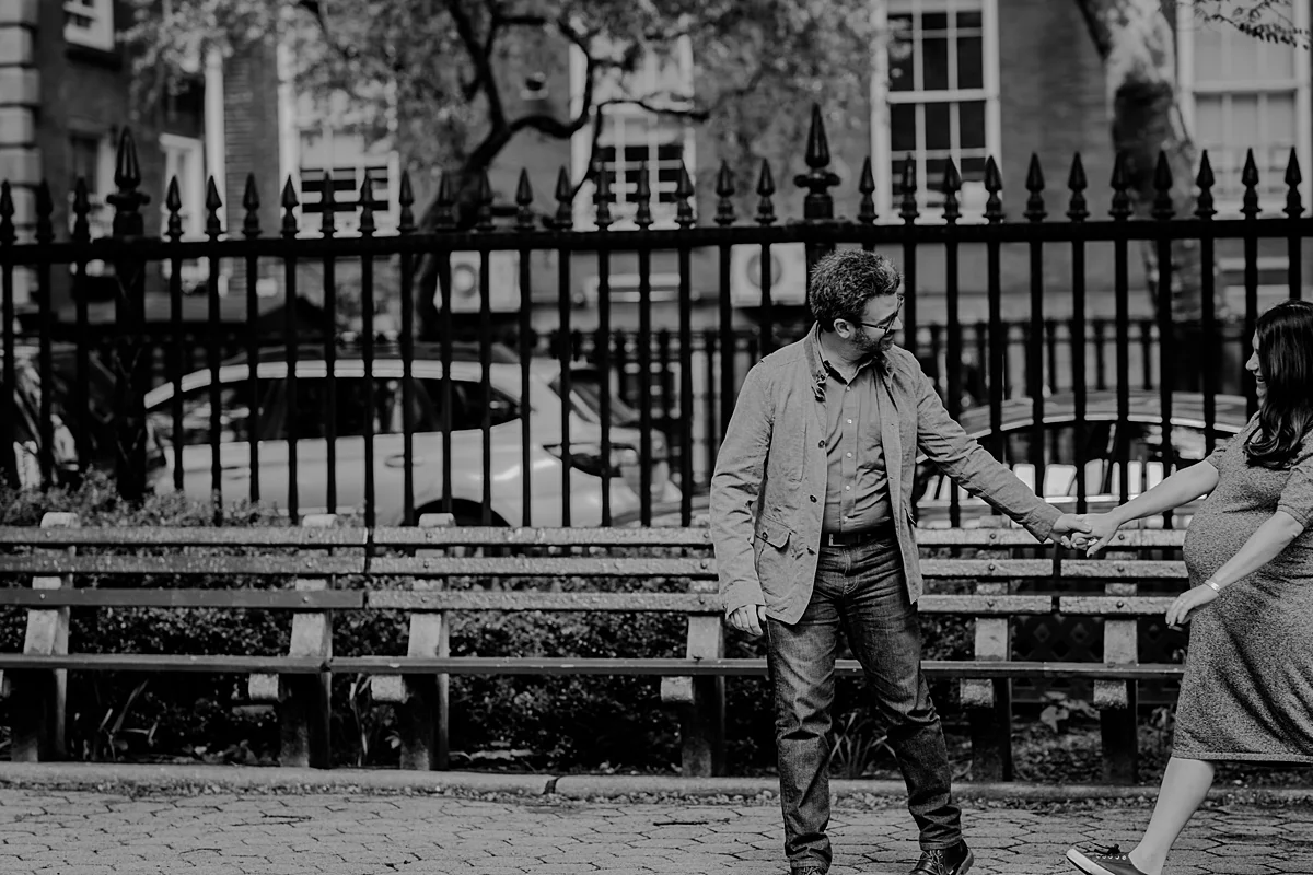 black and white image of husband and wife holding hands and having fun during a park stroll during their nyc maternity photo session. photo by nyc family and newborn photographer krystil mcdowall