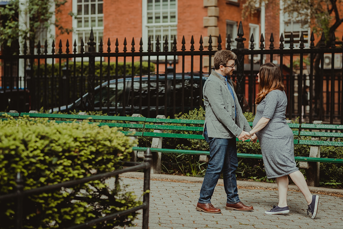 image of husband and wife in the park and holding hands looking into each other's eyes during their nyc maternity photo session. photo by nyc family and newborn photographer krystil mcdowall