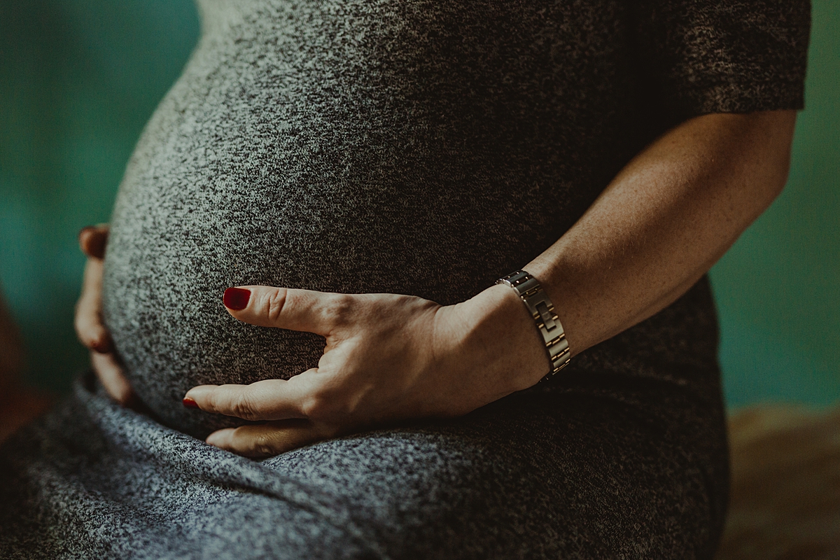 close up maternity portrait of expecting mother's pregnant belly in black and white dress while she's sitting in her bedroom during maternity photo session. photo by nyc family and newborn photographer krystil mcdowall