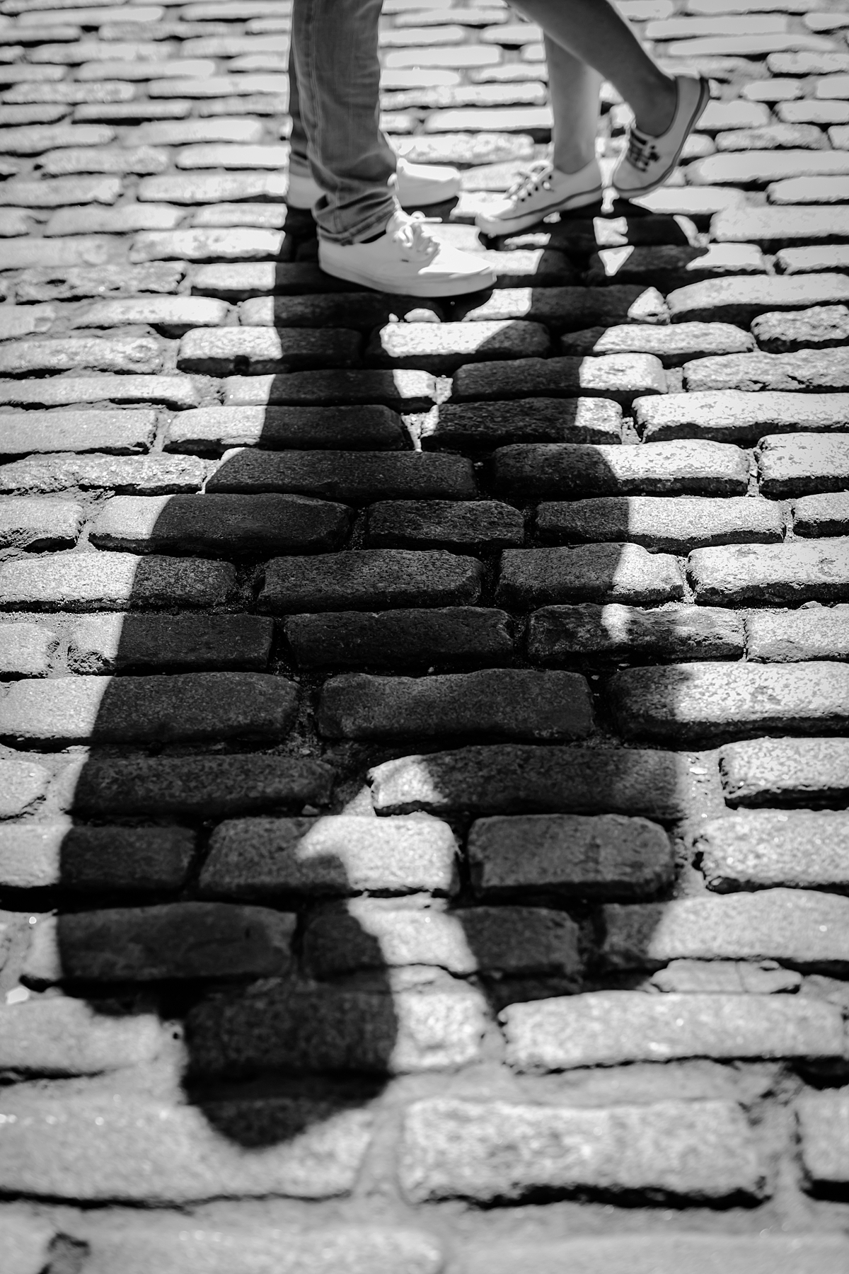 Black and white photo of couple's feet and full body shadow standing on a cobble stoned street during their maternity photo shoot in brooklyn. image by nyc family and newborn photographer krystil mcdowall