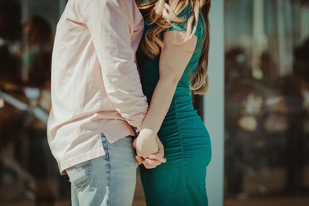 photo of pregnant husband and wife holding hands in front of jane's carousel during outdoor maternity photo session. image by krystil mcdowall photography