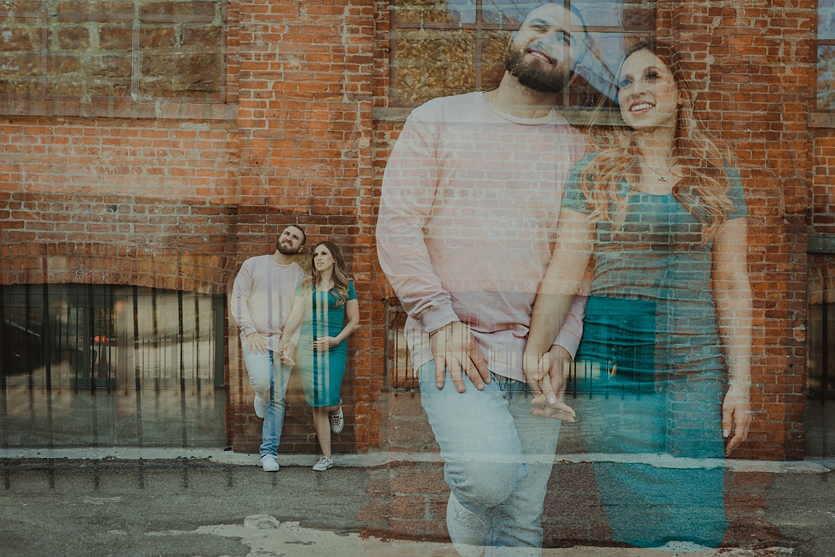 double exposure photo of husband and wife looking out at the manhattan skyline while leaning again gritty brick wall in dumbo brooklyn during maternity photo shoot. image by krystil mcdowall photography