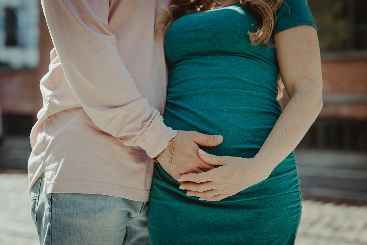 close up image of husband and wife holding pregnant belly during outdoor maternity photo session in dumbo. image by krystil mcdowall photography