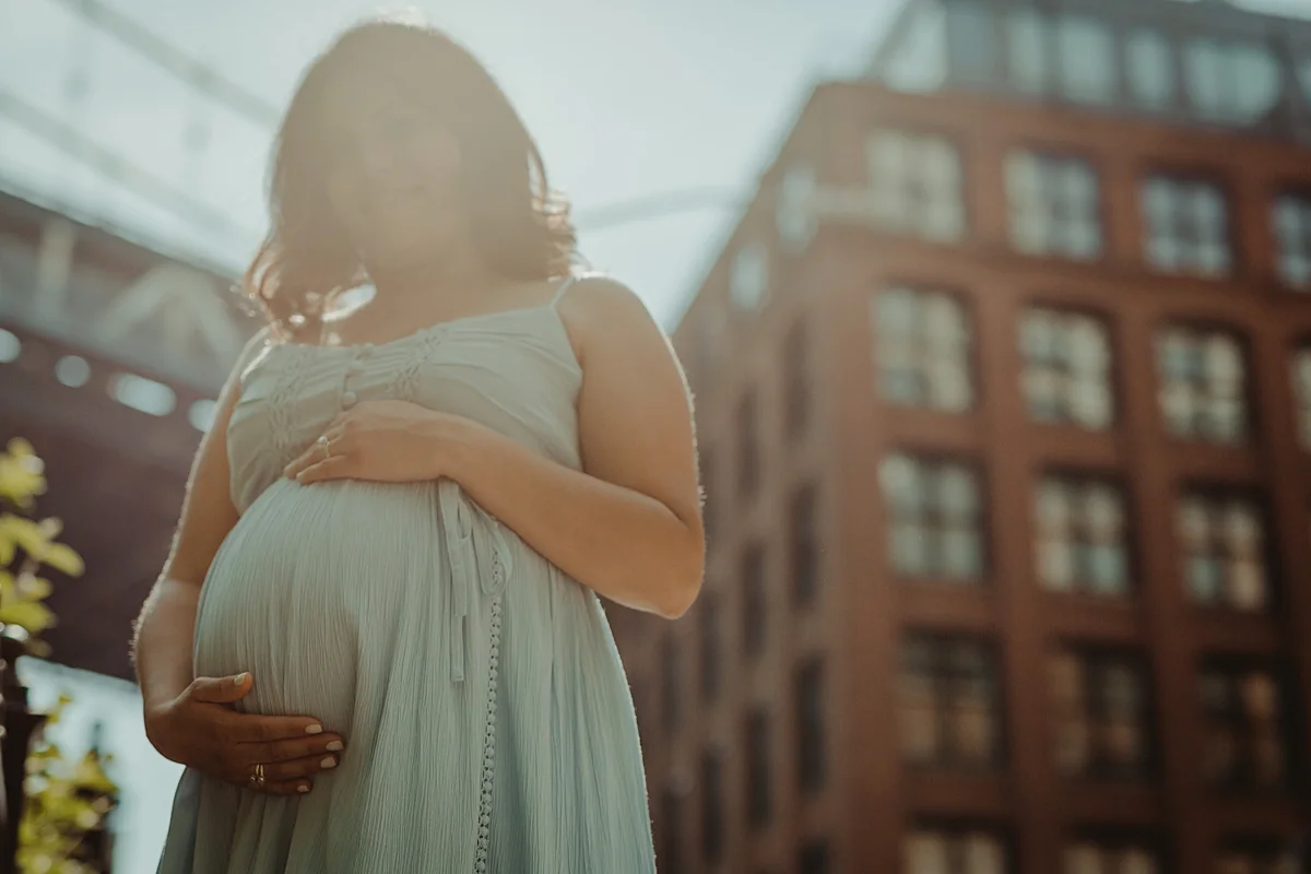 portrait of expecting mom in light blue maternity dress holding her pregnant tummy during outdoor maternity photo session with orange county family photographer krystil mcdowall