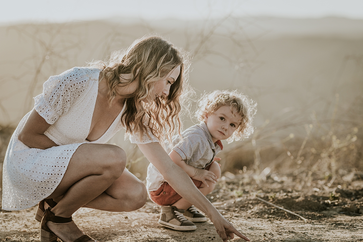 photo by Orange County family photographer Krystil McDowall. Candid photo of boy and his mom playing in the dirt at the mountain top during family lifestyle photo session at Top of the World Laguna Beach California