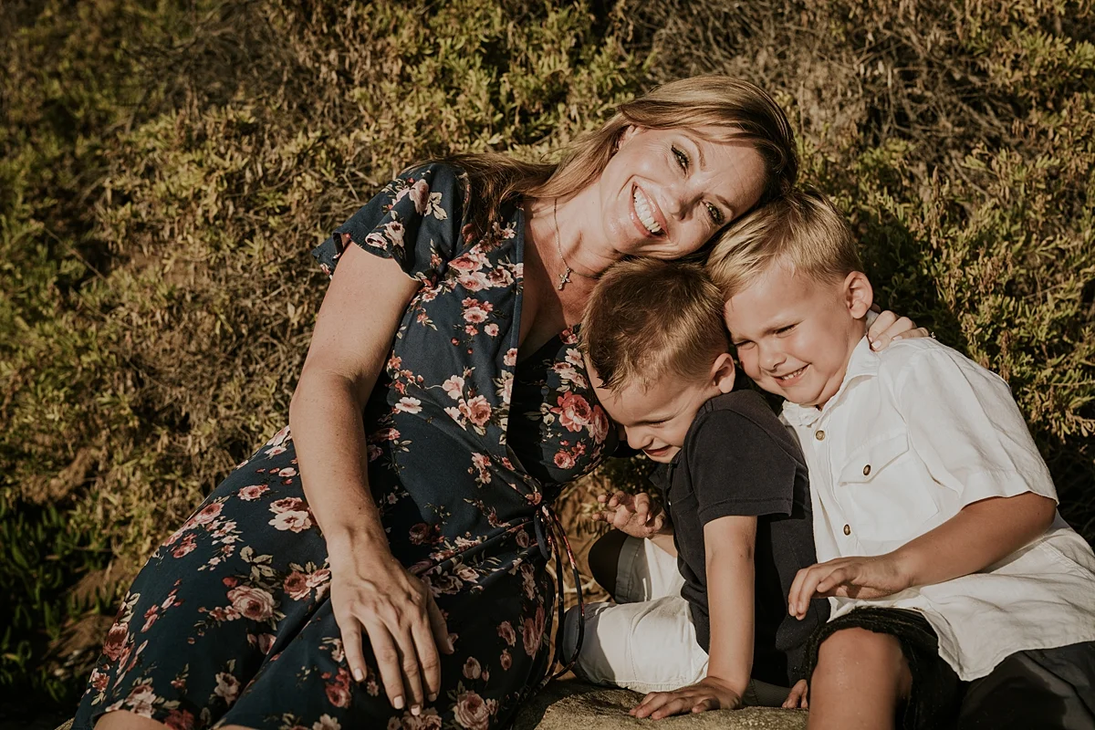 orange county family photographer. photo of mom and her two boys sitting in front of colorful beach cliff during outdoor family photo session at Corona del Mar State Beach with Krystil McDowall Photography