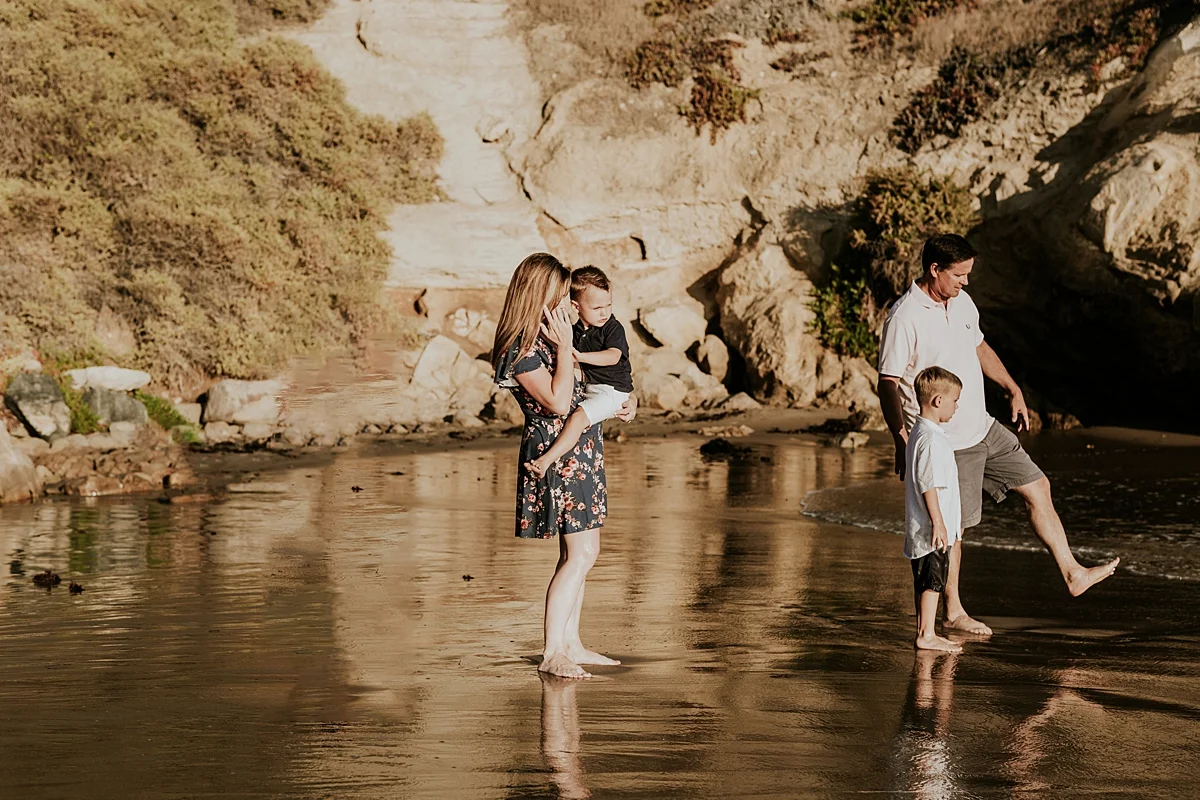orange county family photographer. family photo of mom, dad and their boys playing in the shallow ocean waves during outdoor family photo session at Corona del Mar State Beach with Krystil McDowall Photography