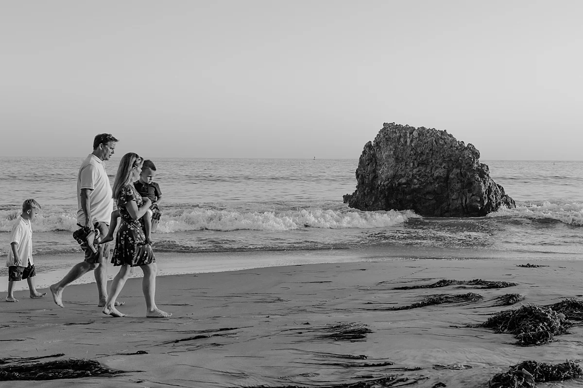 orange county family photographer. candid black and white photo of family as they walk along the beach during outdoor family photo session at Corona del Mar State Beach with Krystil McDowall Photography
