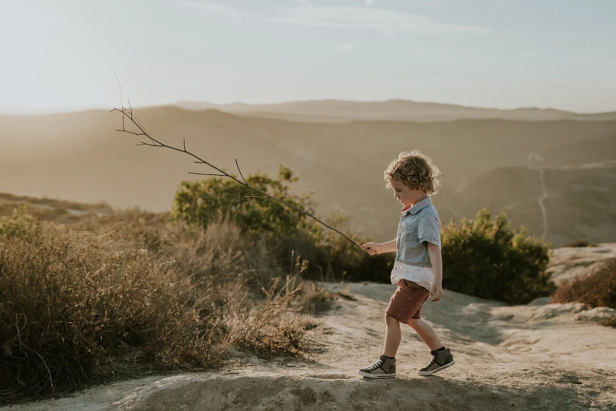 orange county family photographer image of young boy walking with a stick at top of the world languna beach california at sunset