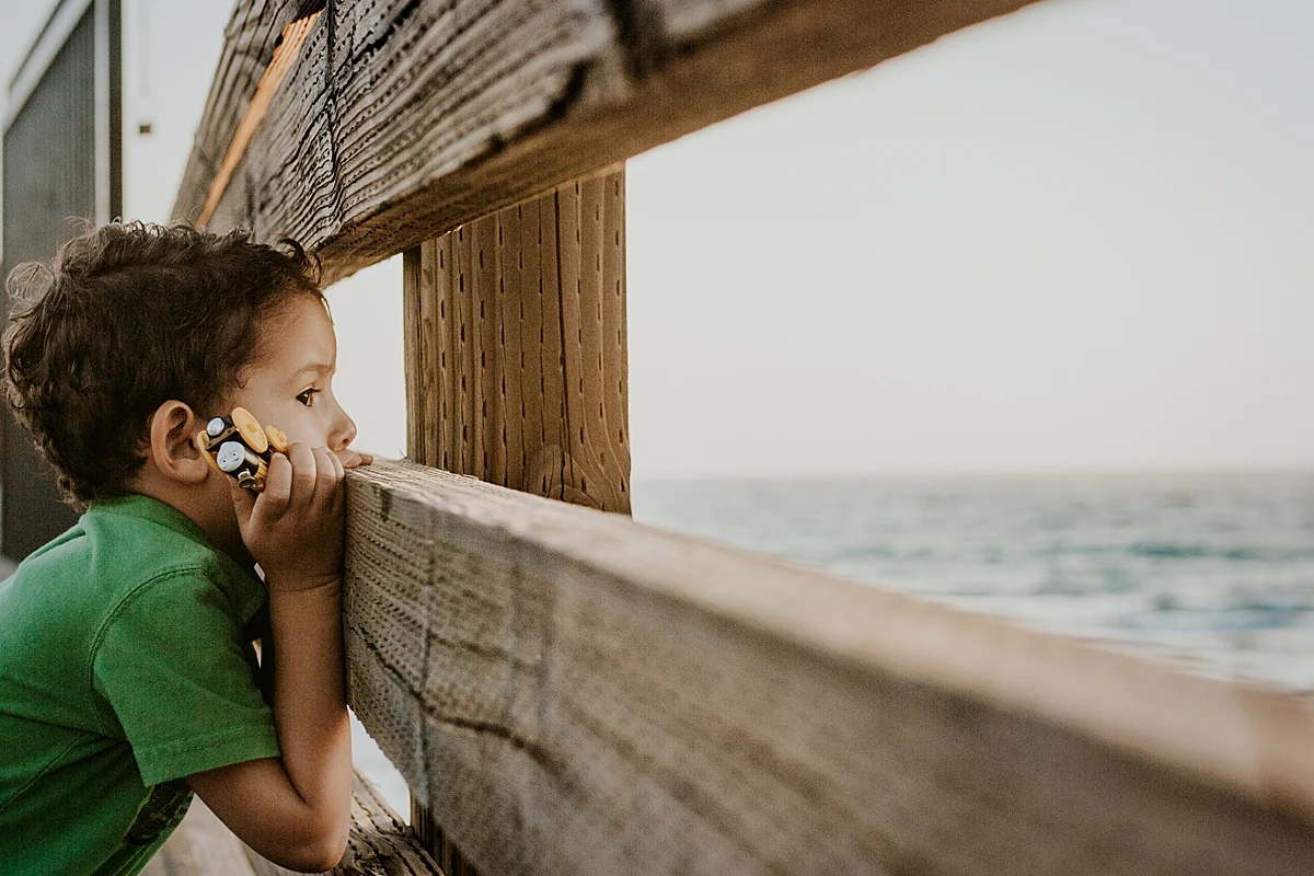 Orange County family photographer. Portrait of young boy looking out to the ocean from the Huntington Beach Pier during outdoor family photo session with Krystil McDowall Photography