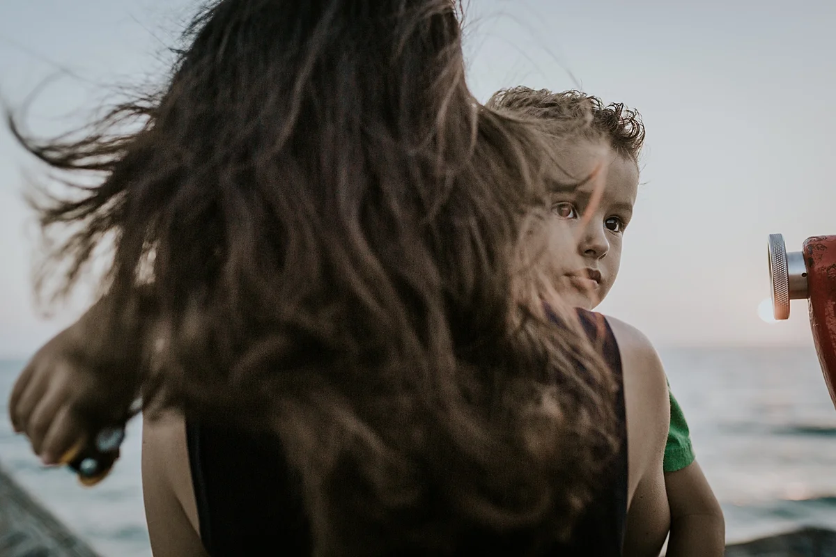 Orange County family photographer. Photo of mom hugging son while looking out at the ocean from the pier at Huntington Beach during family photo shoot with Krystil McDowall Photography