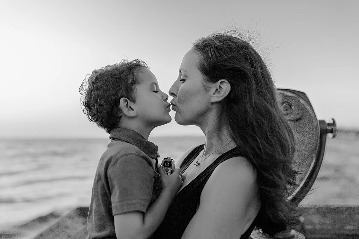 Orange County family photographer. Photo of mom kissing her eldest son on the pier at Huntington Beach during family photo shoot with Krystil McDowall Photography