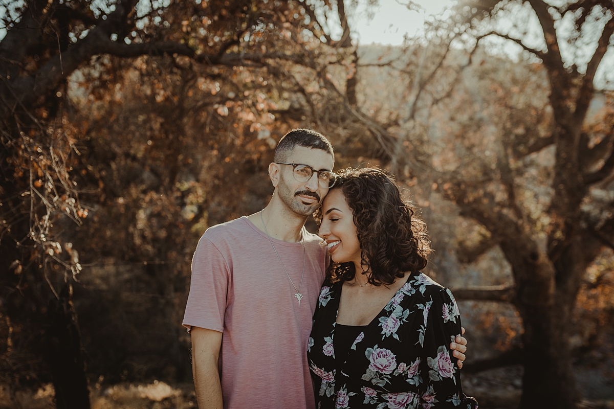 Orange County family photographer. Photo of married couple standing amongst beautiful trees with sun streaming in during outdoor couples photo session in Irvine Regional Park