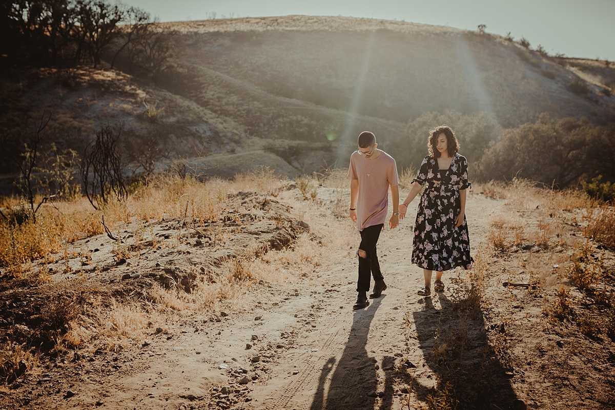 Orange County family photographer. Image of couple walking up hill at at Irvine Regional Park with sun streaming in the background