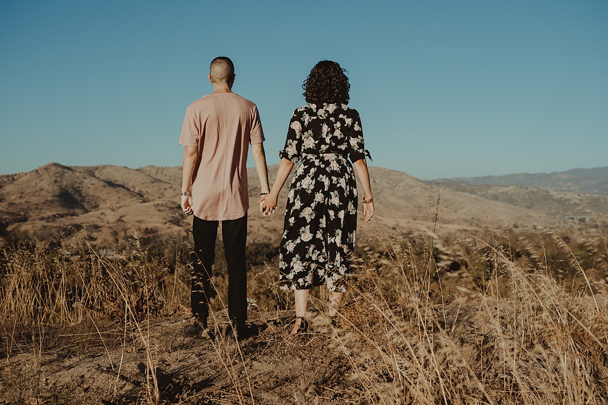 Orange County family photographer. portrait of couple standing away from the camera and looking out at the hills while holding hands at Irvine Regional Park Orange County