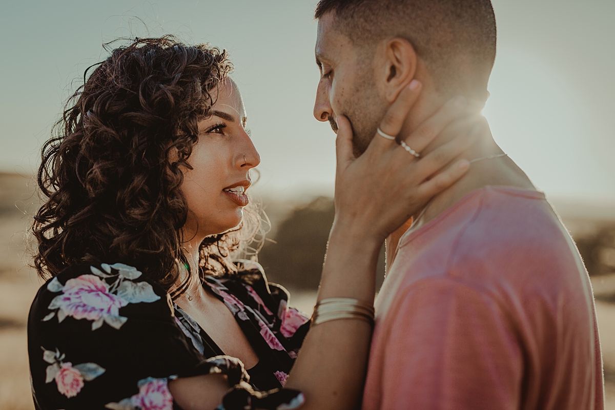 Orange County family photographer. backlit photo of married couple standing among embracing each other while standing in the fields at sunset during couple's photo session at Irvine Regional Park