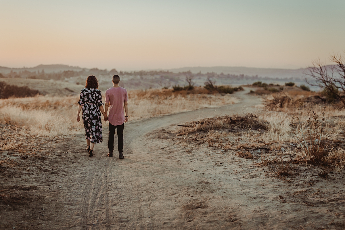 Orange County family photographer. photo of couple walking hand in hand along dirt road into the sunset at Irvine Regional Park Orange County