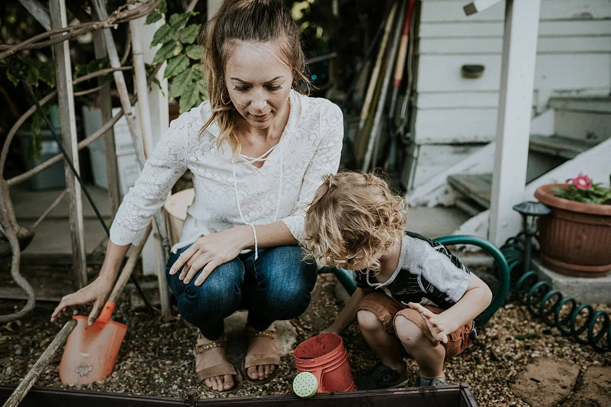 Orange County family photographer. Photo of young curly boy and his mama holding watering cans in their front yard during documentary photo session with Krystil McDowall Photography