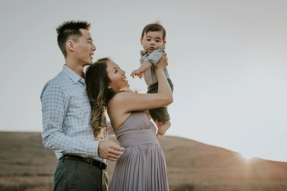 Orange County family photographer. photo of mom and dad holding their baby boy in the air in the yellow fields at Quail Hill Trailhead in California