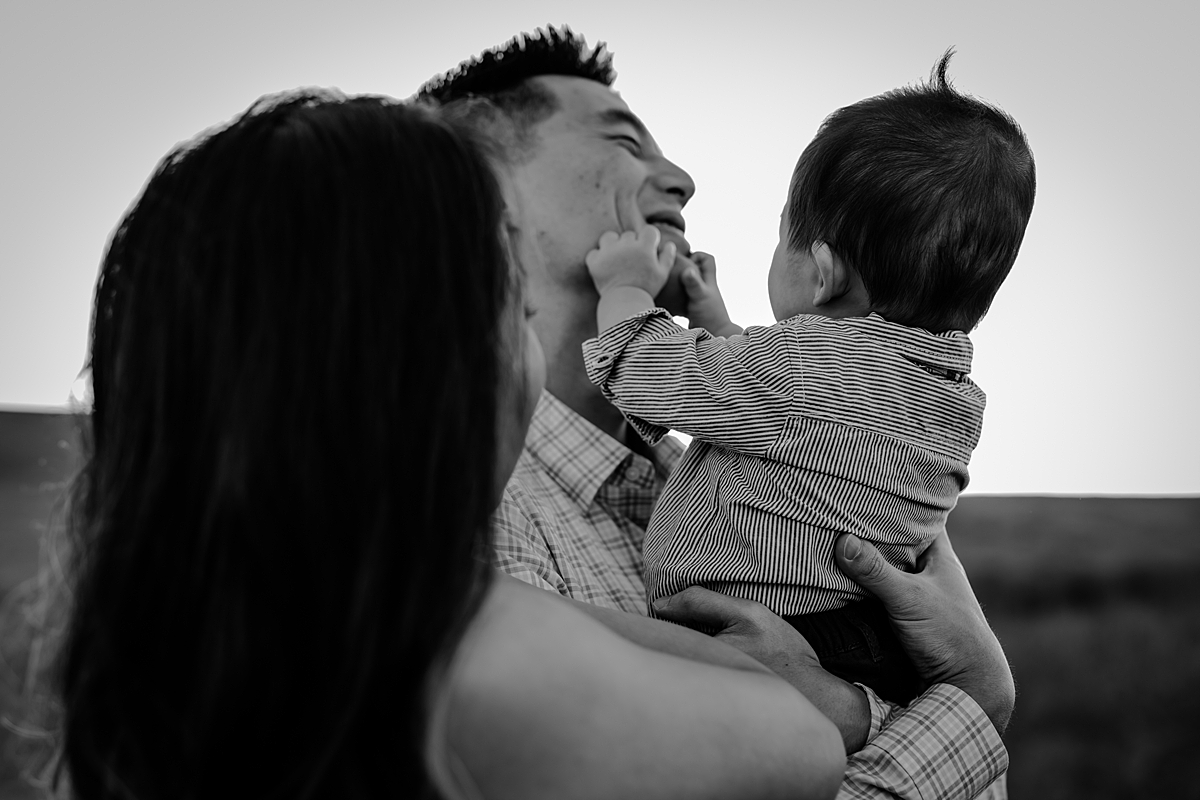Orange County family photographer. Candid black and white photo of baby boy grabbing onto dad's face during family photo shoot at Quail Hill Trailhead in California