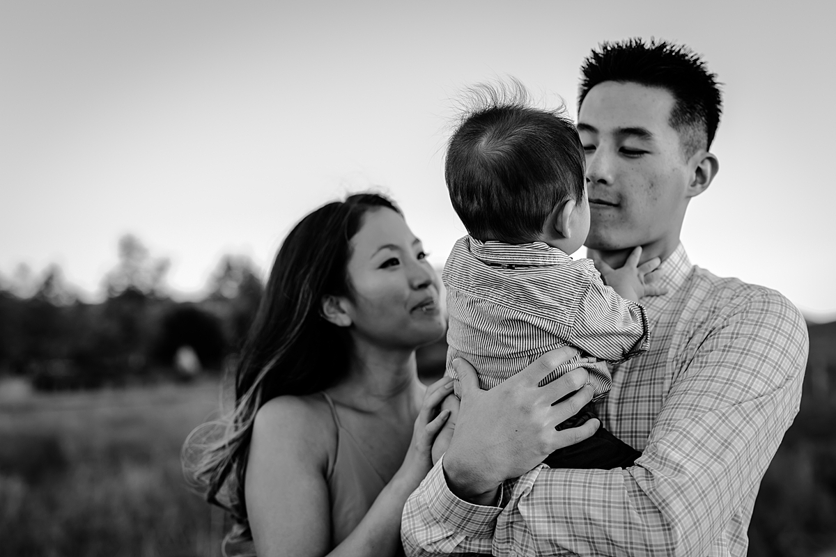 Orange County family photographer. black and white photo of mom and dad holding their baby son as he looks into dad's eyes during family photo shoot at Quail Hill Trailhead in California