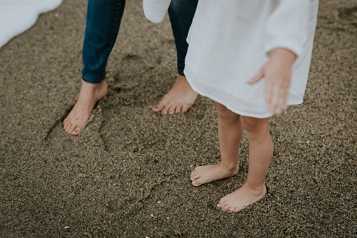 Orange County family photographer. Mom and daughter rub their bare feet in the sand at Table Rock Beach, Laguna Beach during family photo session with Krystil McDowall Photography